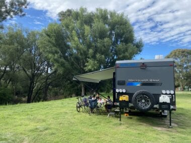 A family sits under the awning of a caravan